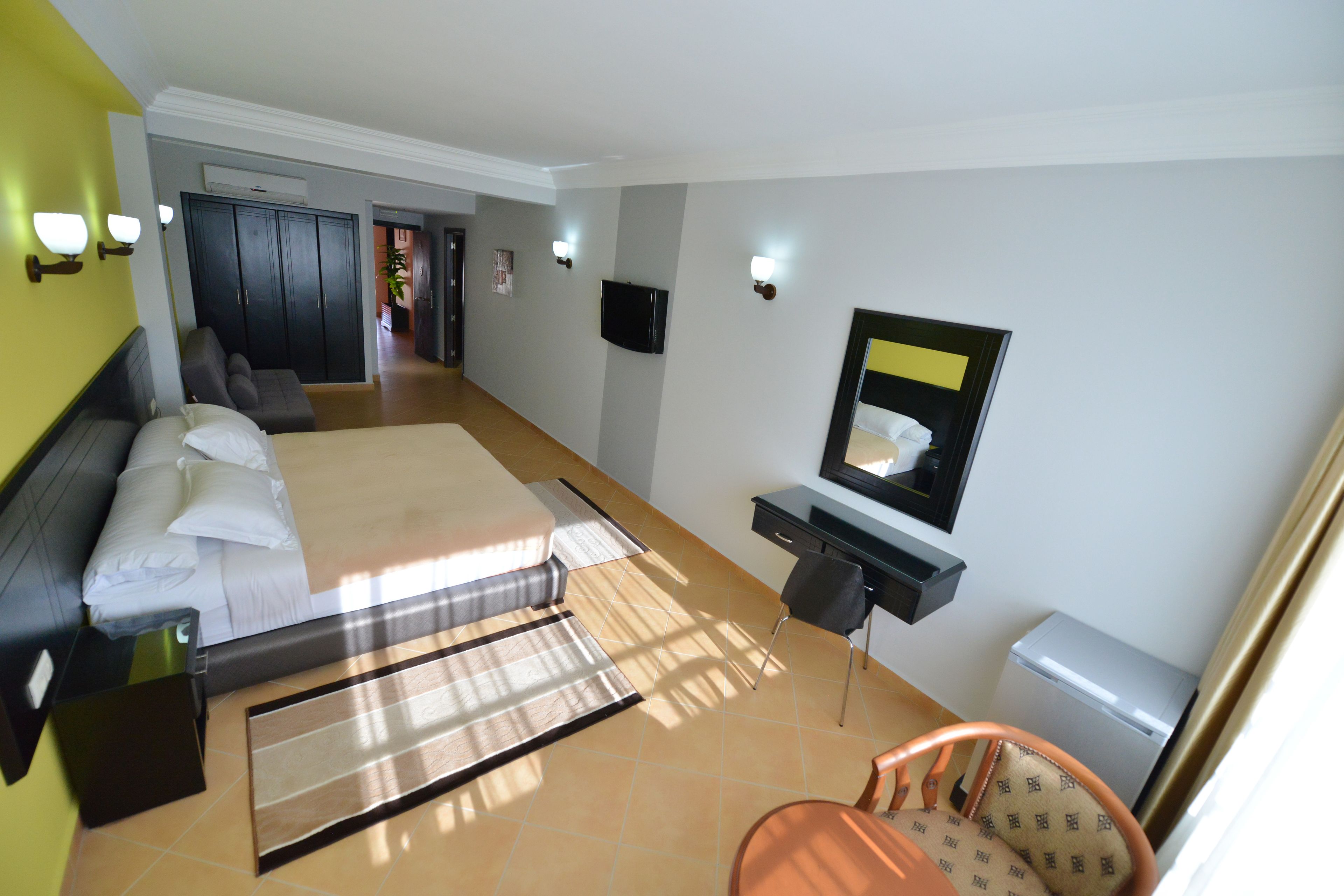 A hotel room with a bed, a desk, a chair, a wardrobe, and a television.