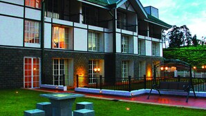 Un hotel de varios pisos con fachada de piedra, ventanas amplias y un área exterior bien iluminada con mobiliario.
