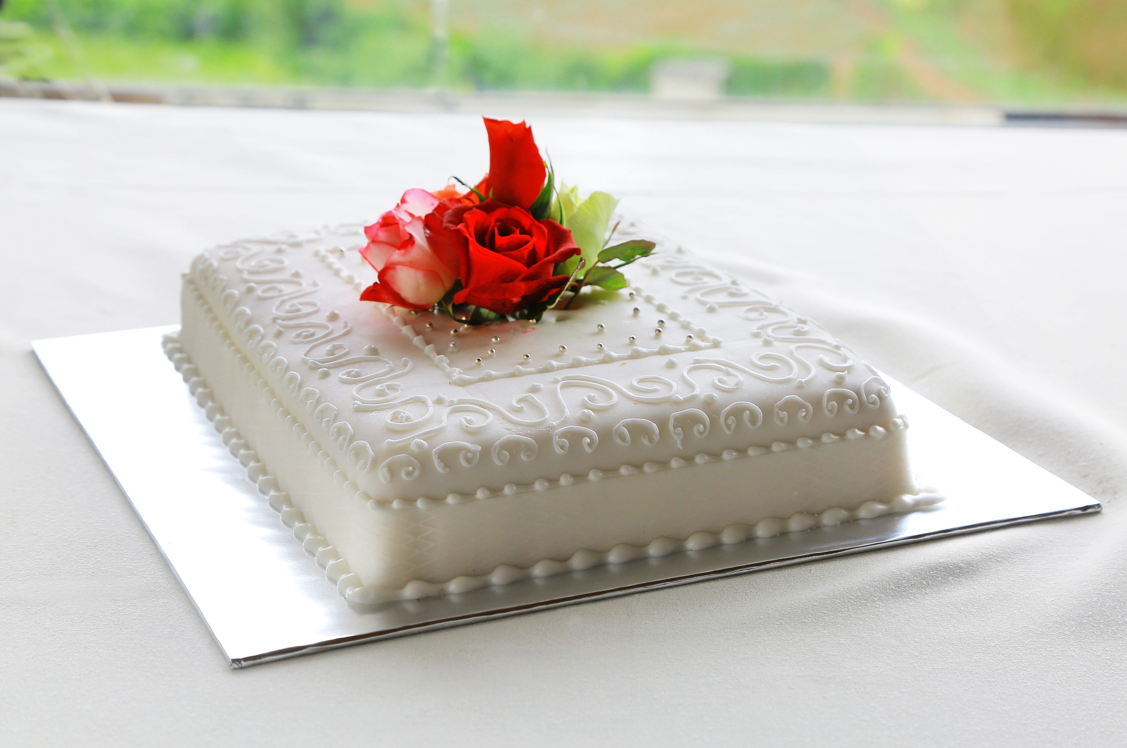 Un pastel blanco con decoración floral sobre una base plateada.