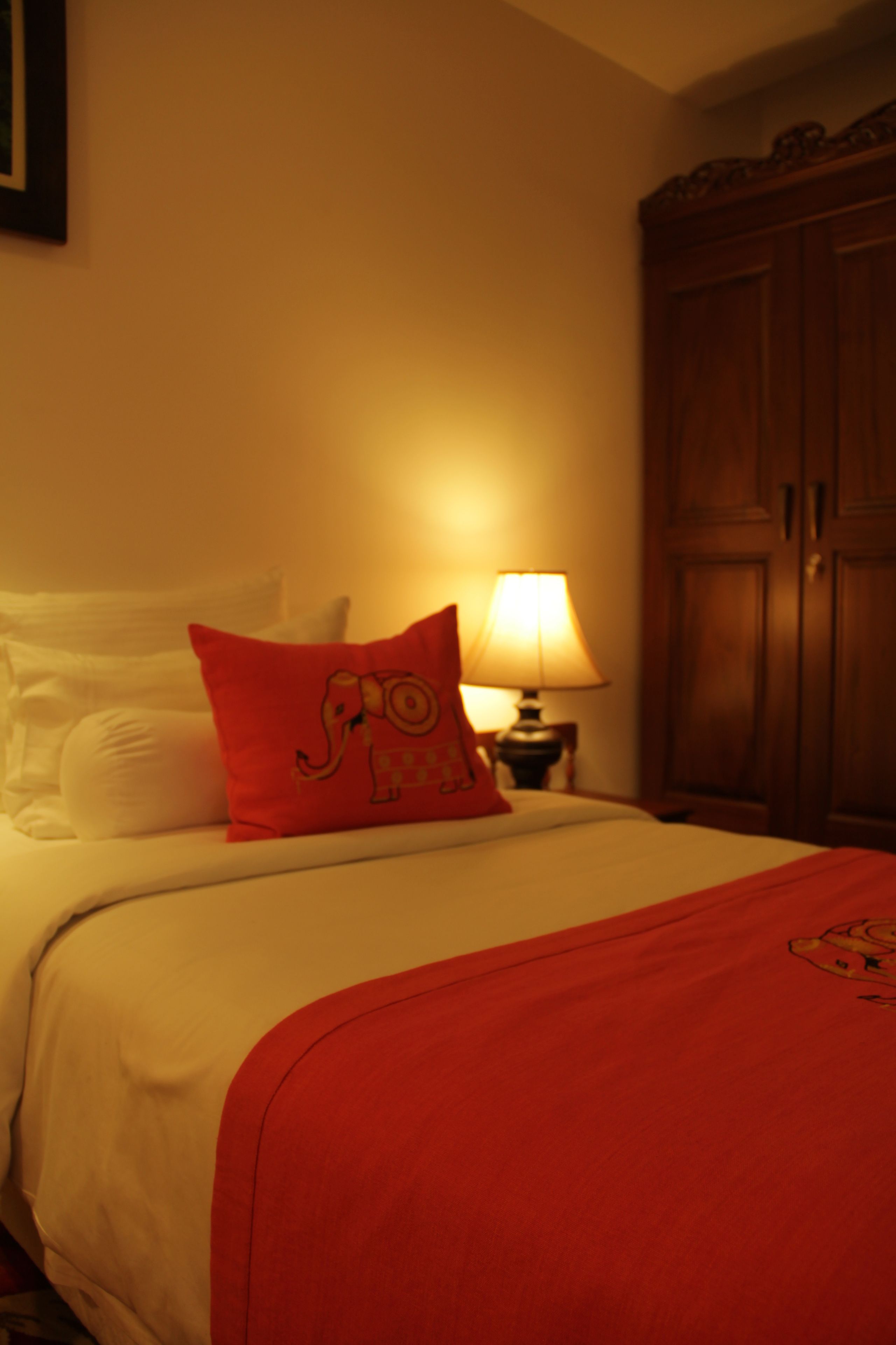 Una habitación de hotel con una cama, almohada roja, lámpara y armario.