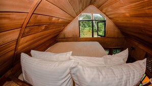Un cuarto de madera acogedor y triangular con una cama y una ventana que da a un jardín exuberante.