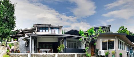 Uma casa moderna com um telhado curvo, uma parede de pedra e um jardim com diversas plantas e um banco.