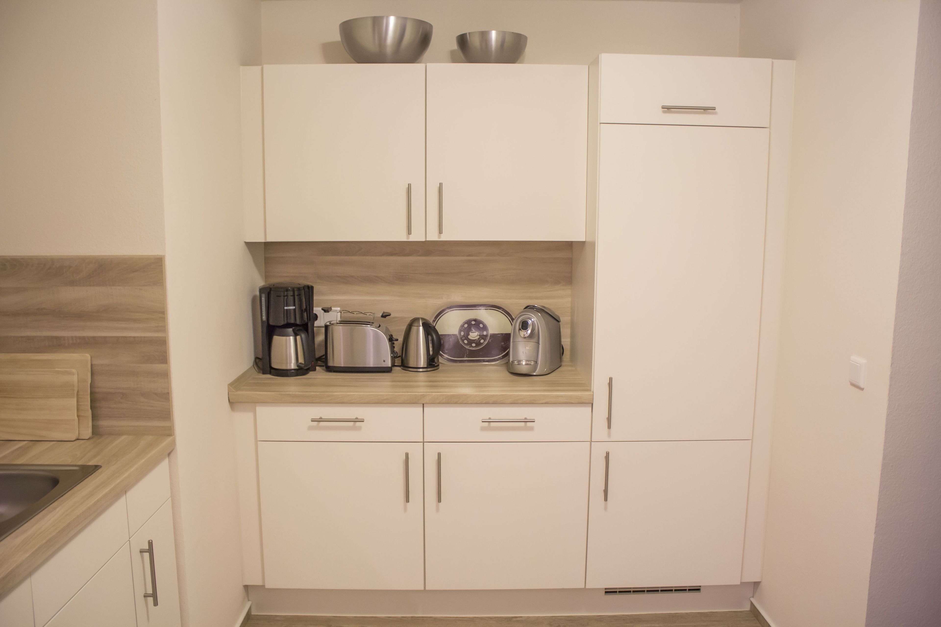 A kitchen with white cabinets, a wooden countertop, and various appliances including a coffee maker, toaster, and kettle.