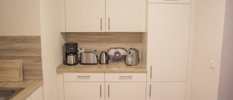 A kitchen with white cabinets, a wooden countertop, and various appliances including a coffee maker, toaster, and kettle.