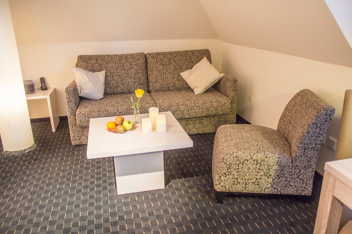 Een knus ingerichte kamer met een gestreept bankje, een bijpassende fauteuil, een klein tafeltje met fruit en kaarsen, en een vloer met een patroon.