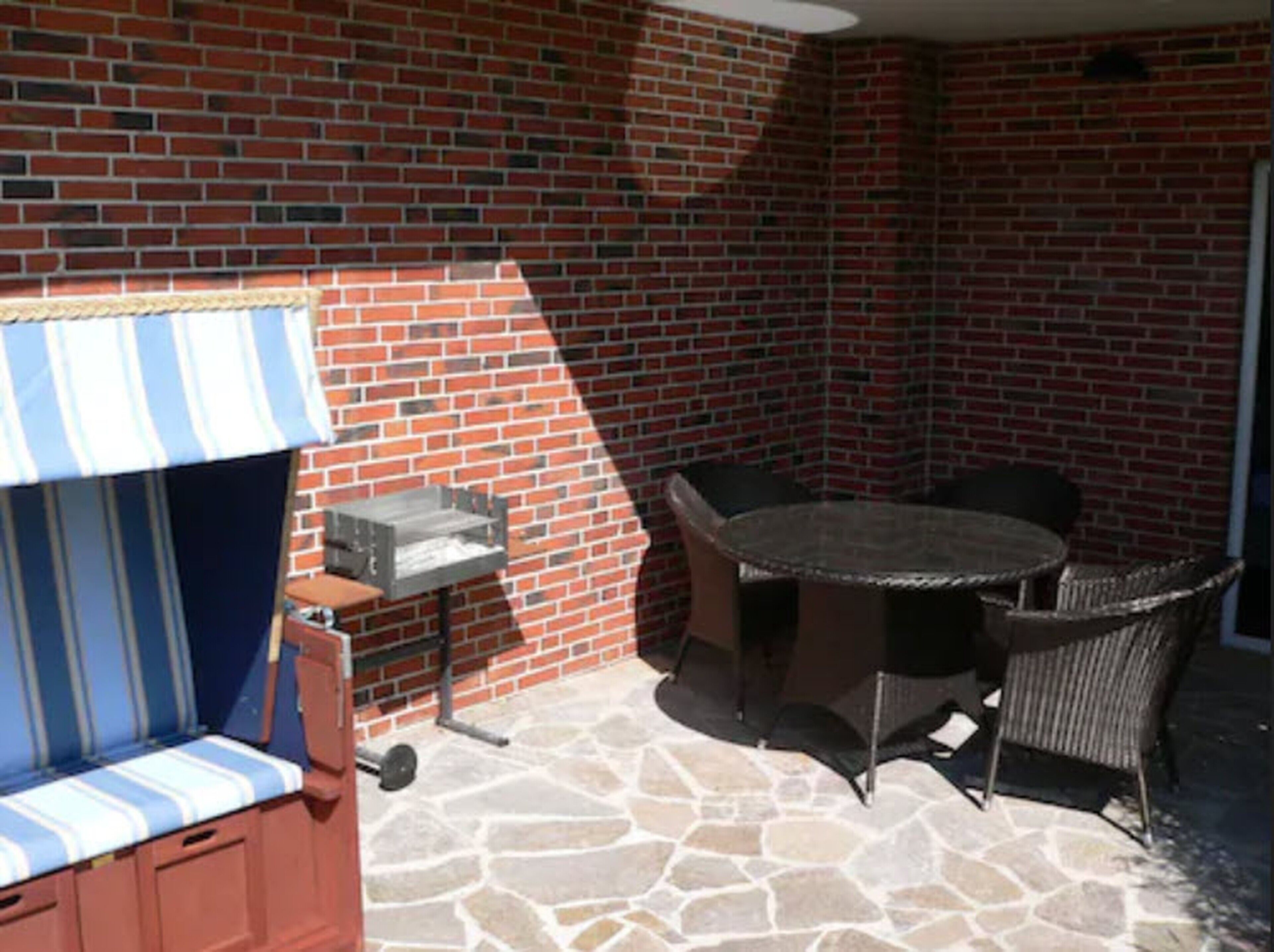 A patio area with a brick wall, a round table with chairs, a cushioned bench, and a grill.