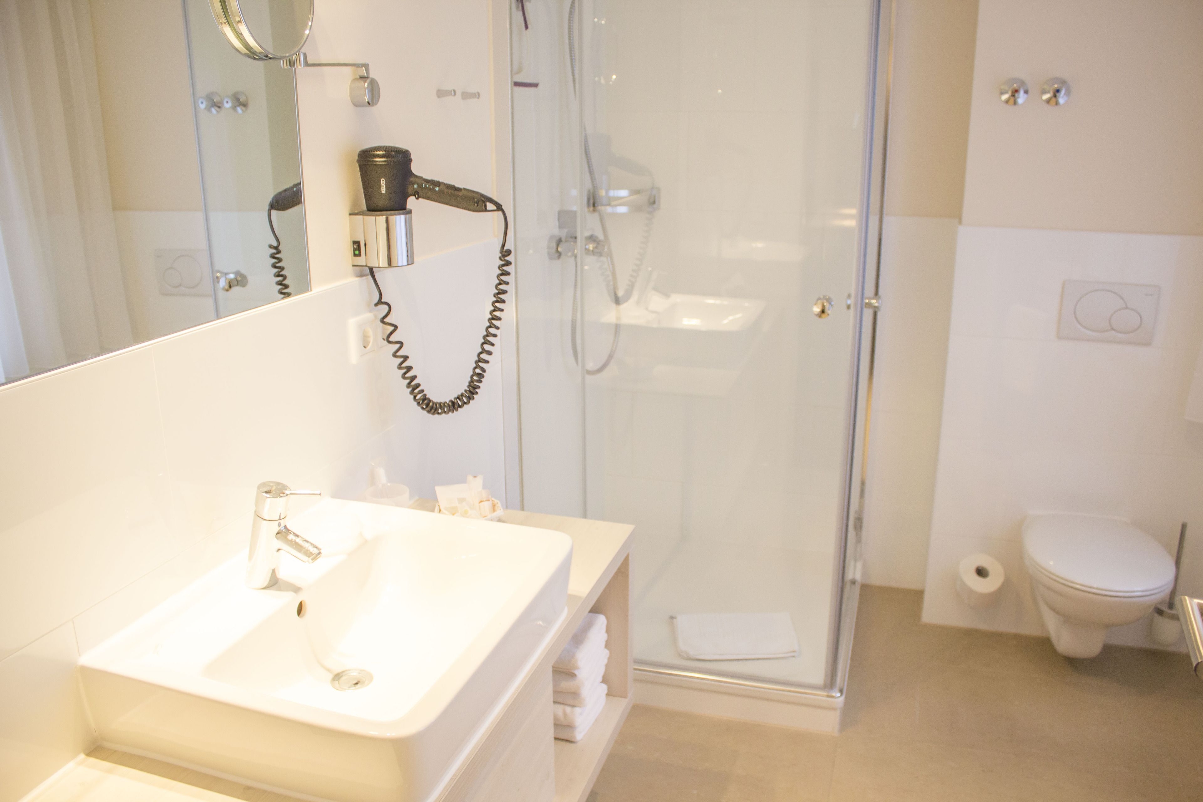 A bathroom with a sink, mirror, hairdryer, shower, and toilet.