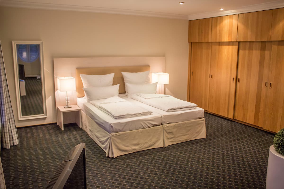Een hotelkamer met een tweepersoonsbed, twee nachtkastjes met lampen, een grote kledingkast en een spiegel.