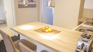 Une petite cuisine avec un plan de travail en bois, un grille-pain et un saladier rempli de fruits. On y trouve deux chaises et un évier.