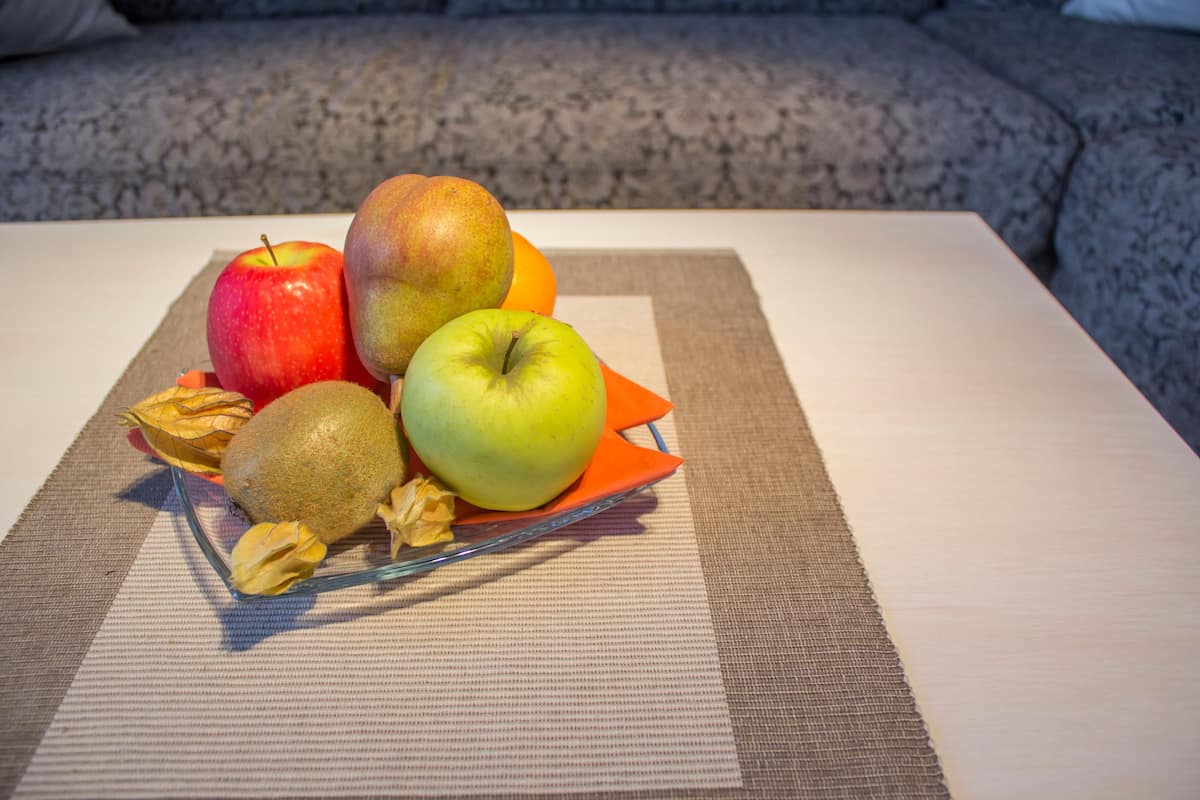 Een tafel met een fruitstuk, met onder andere appels, een kiwi en een sinaasappel.