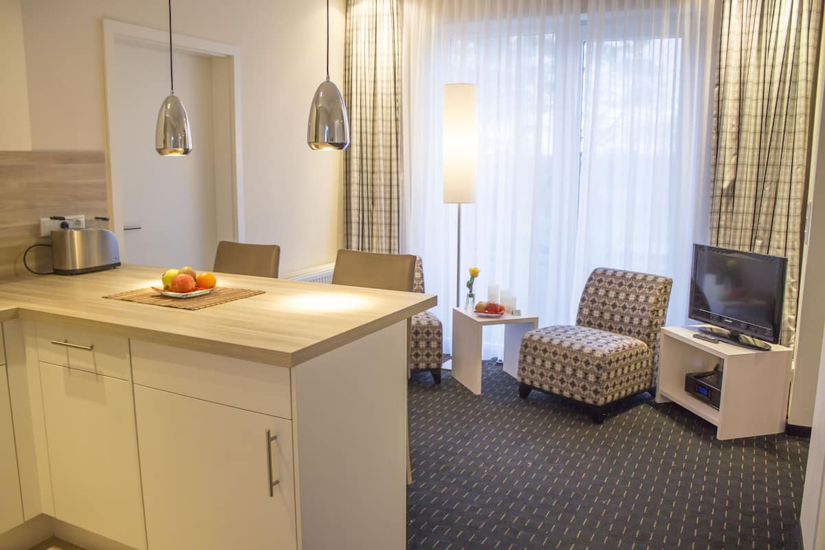 Een hotelkamer met een houten eettafel, twee gestreepte fauteuils, een bank, een televisie op een standaard en een groot raam met gordijnen.