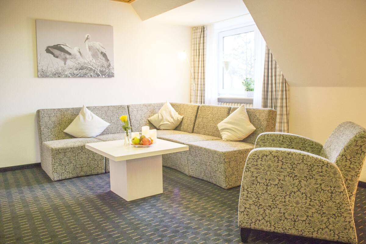 Een woonkamer met een bank, een fauteuil, een salontafel en een schilderij aan de muur.