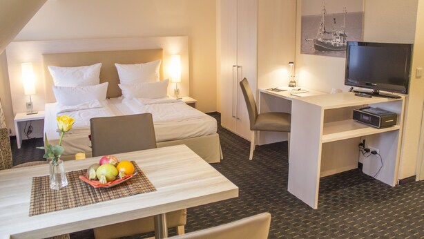 Une chambre d’hôtel équipée d’un lit, d’un bureau, d’une chaise, d’une télévision et d’un panier de fruits.