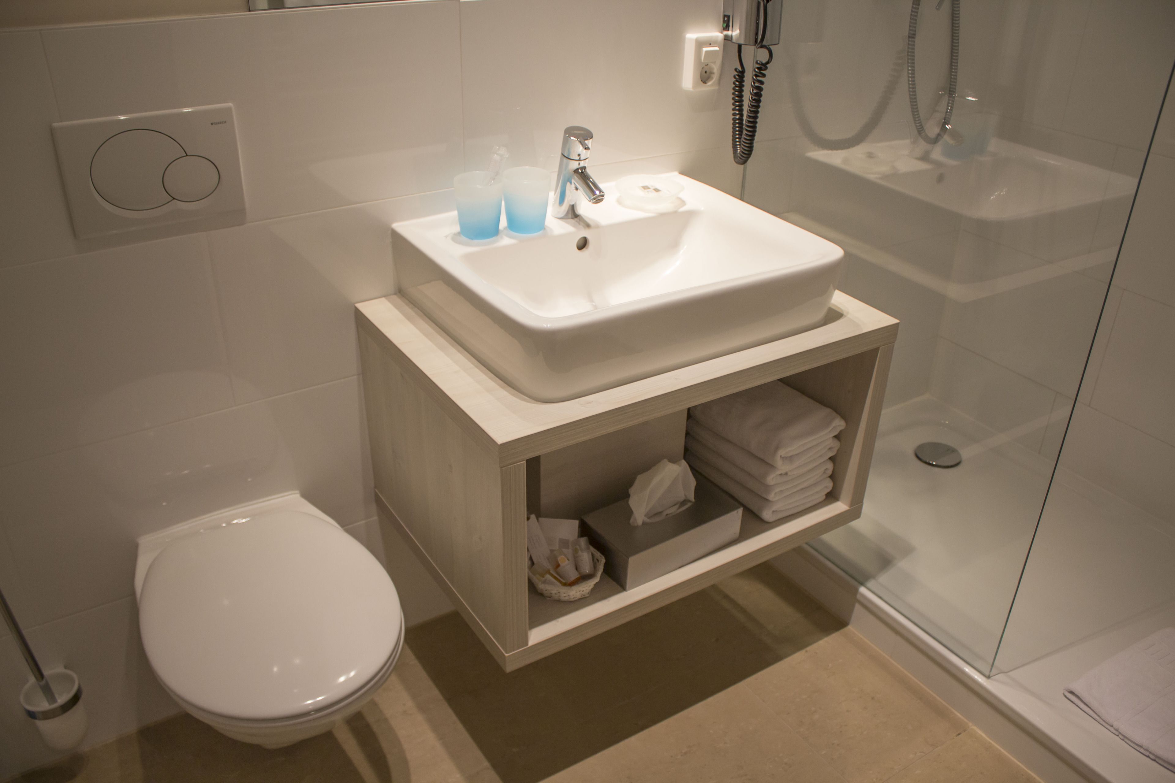 Casa de banho moderna com lavatório branco, sanita e chuveiro com parede de vidro.