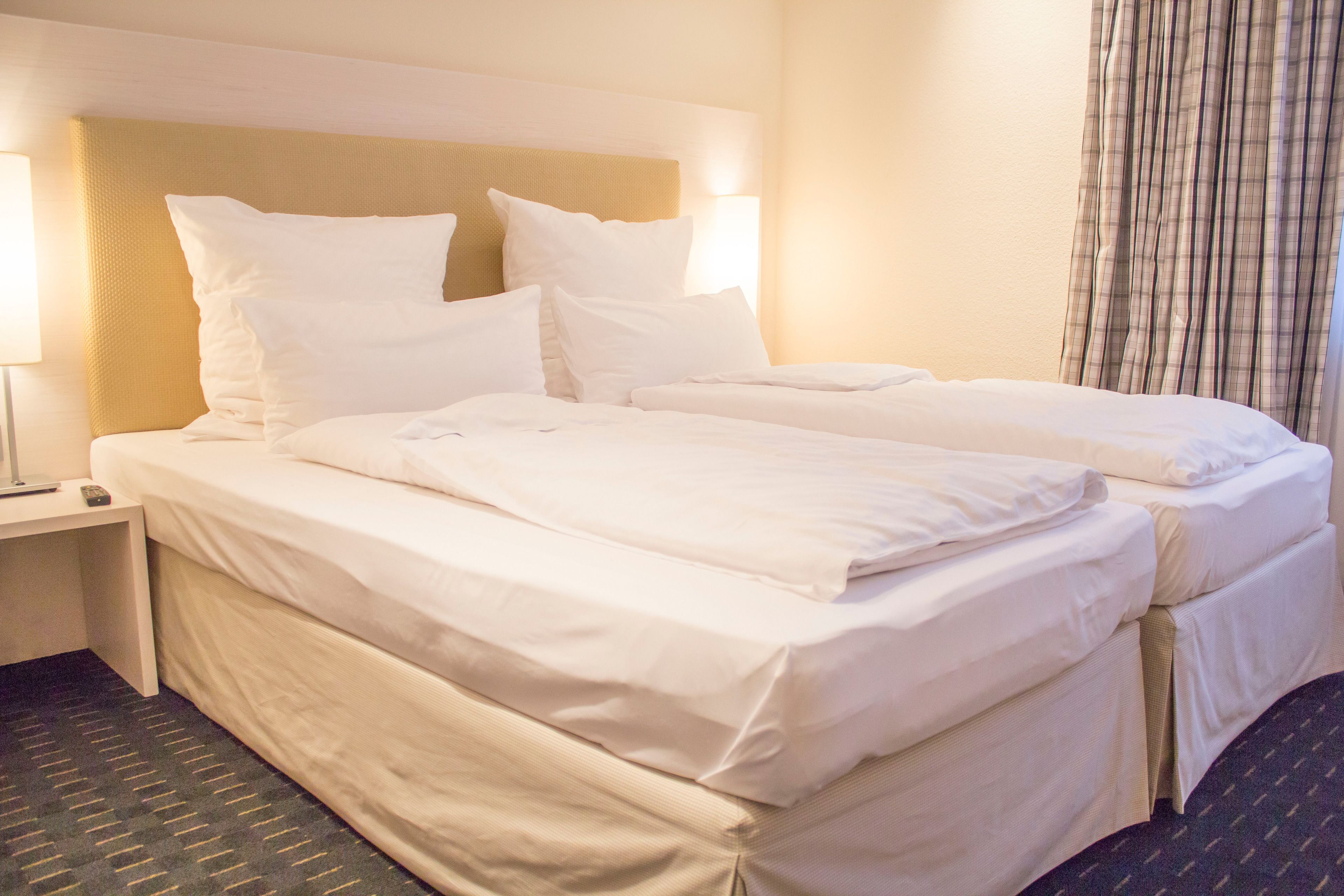 A hotel room with two beds, a nightstand, and a lamp.