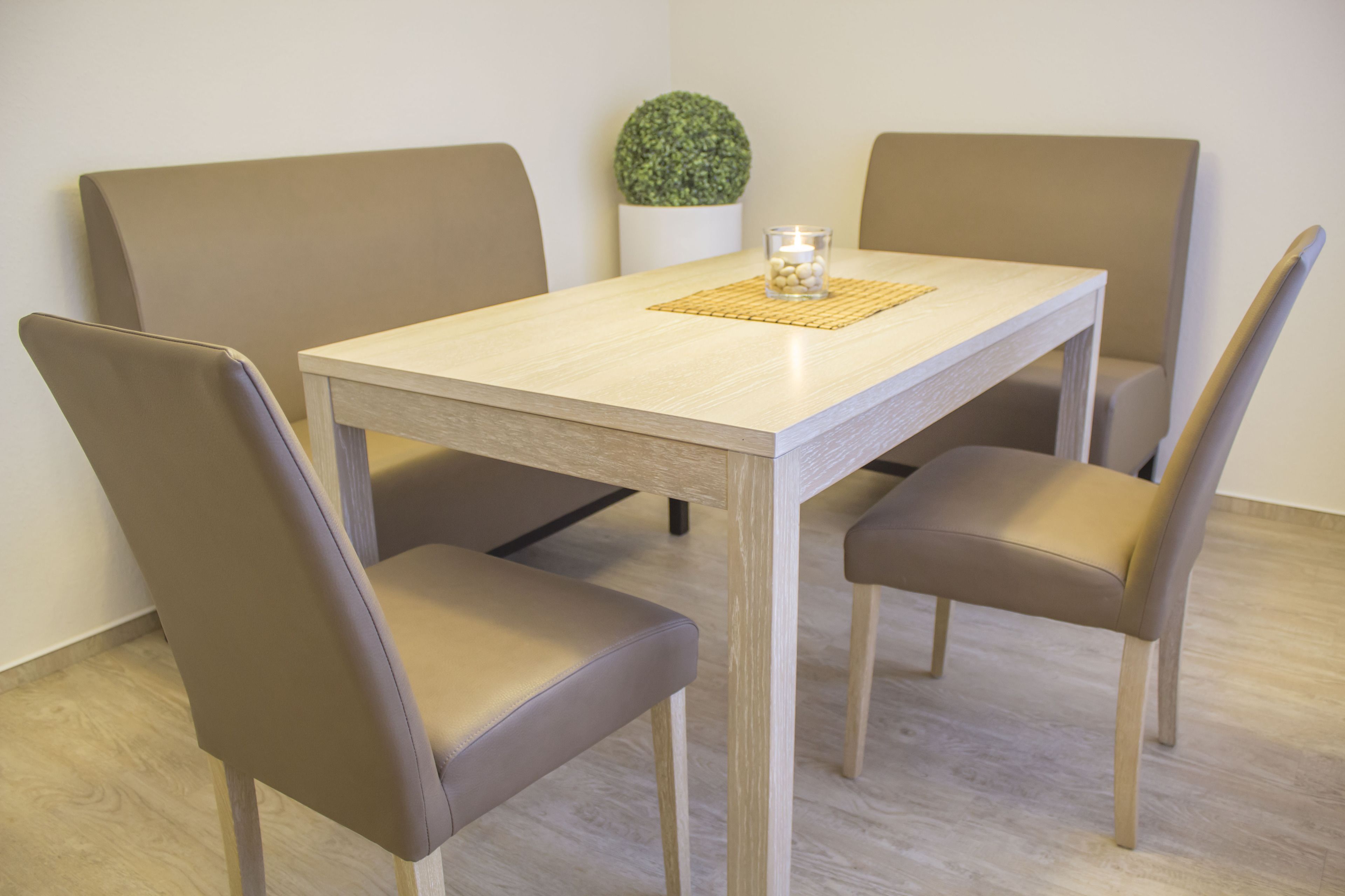 Een eettafel met vier stoelen, een kleine potplant en een kaars op een placemat.