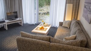 Un salon avec un canapé, une table basse sur laquelle se trouvent des fruits, un téléviseur et une vue sur un jardin, visible à travers une porte vitrée.