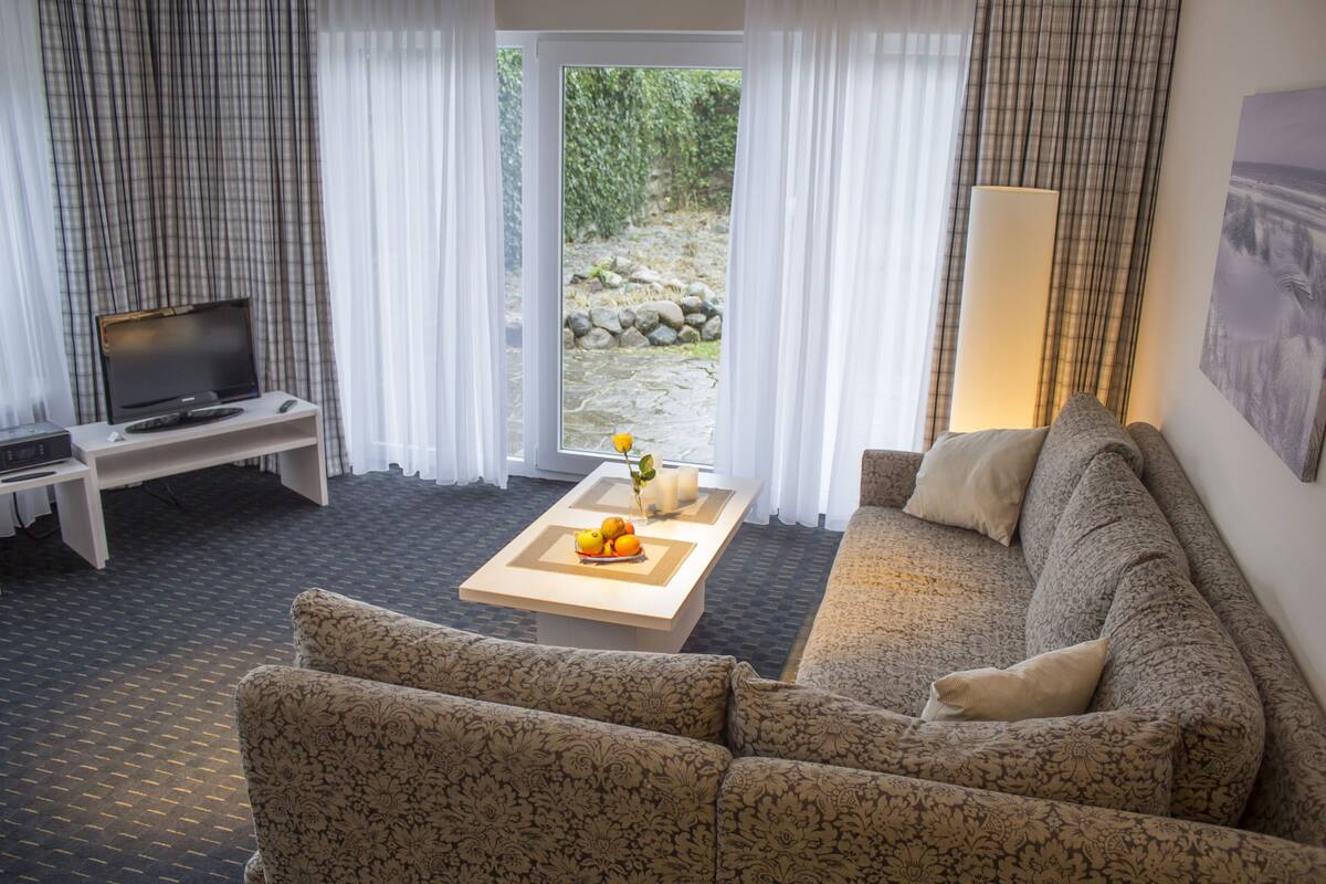 Een woonkamer met een bank, een bijzettafeltje met fruit, een televisie en uitzicht op een tuin door een glazen deur.