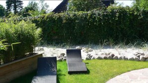 Deux fauteuils de jardin sont placés sur une pelouse verdoyante, avec un chemin de pierres et une haie en arrière-plan.