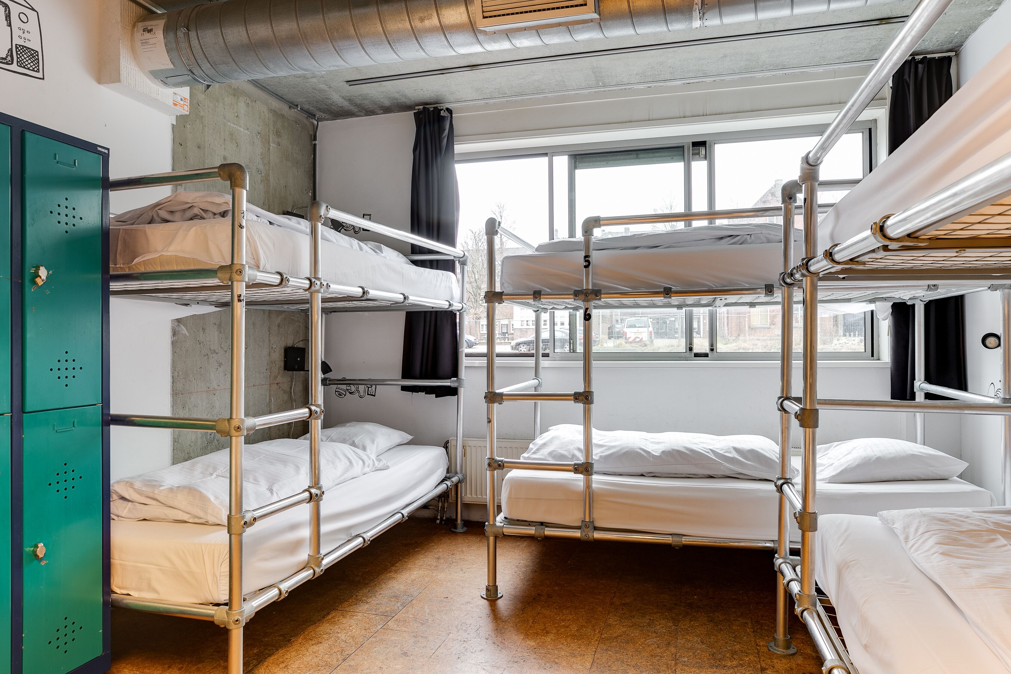 Ein Schlafsaalzimmer mit Etagenbetten, einem grünen Stauraumschrank und einem Fenster mit Stadtblick.