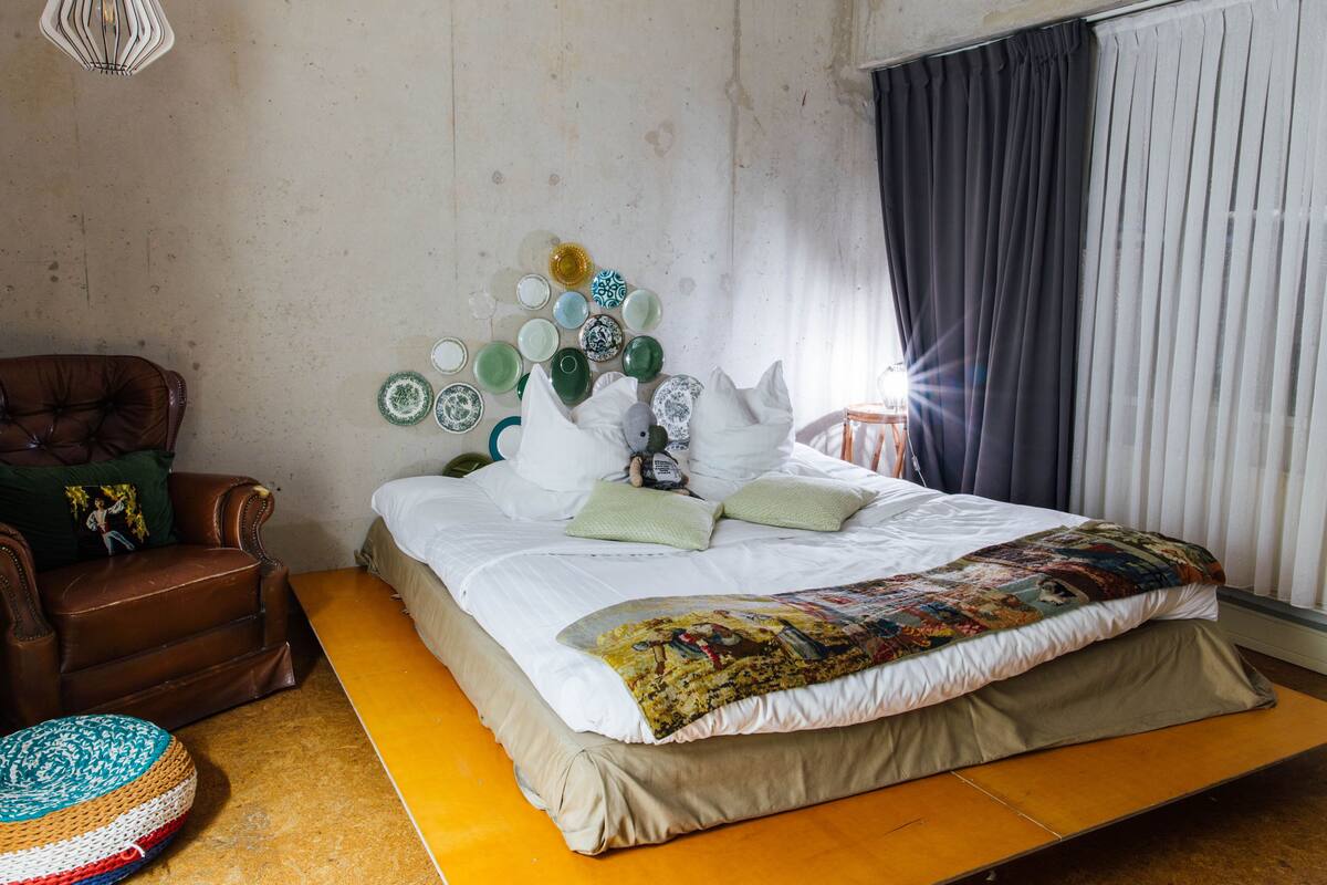 A bedroom with a bed, a brown leather chair, a small round rug, and a wall with a collection of plates.