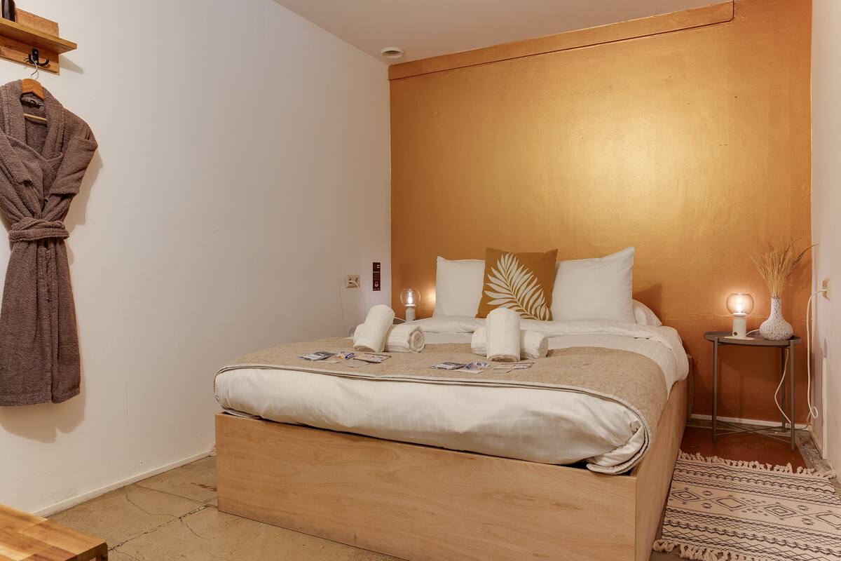 A neatly made bed with towels, a bedside lamp, and a small table with a vase.