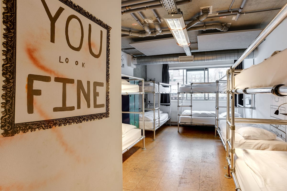 A dormitory room with bunk beds, a sign on the wall, and a window providing natural light.