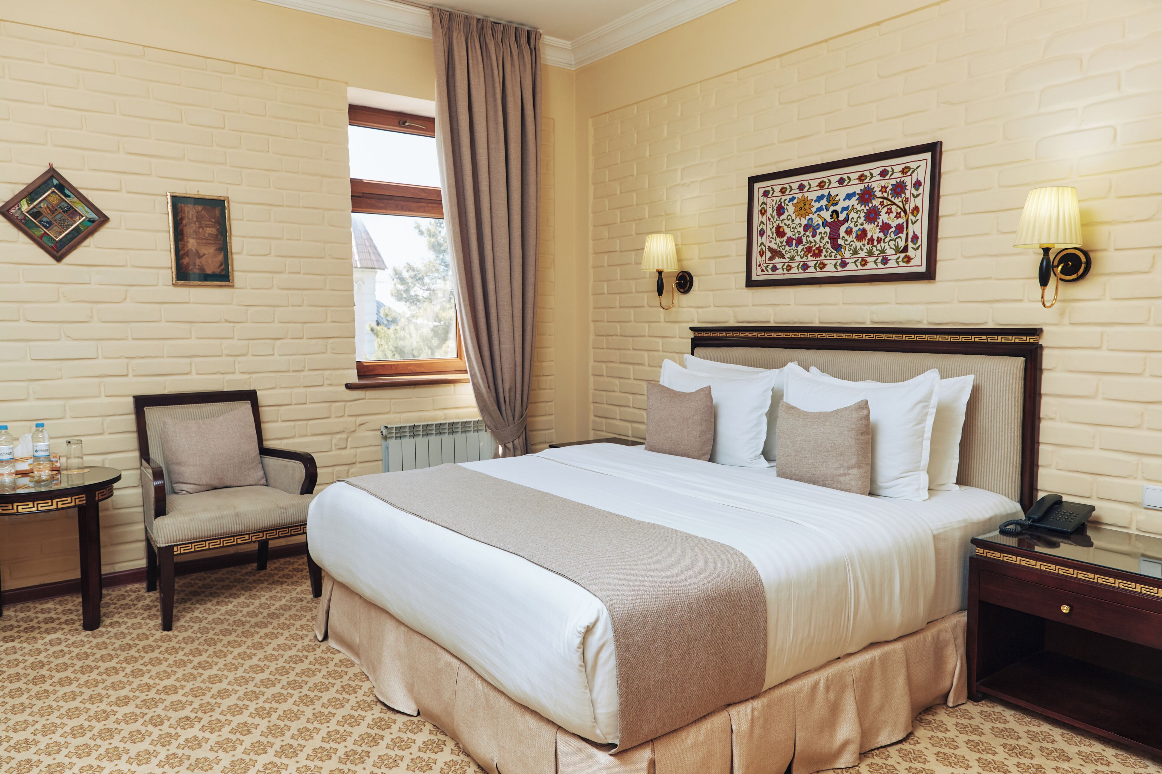 A hotel room with a large bed, a chair, a nightstand, a lamp, and a window with curtains.