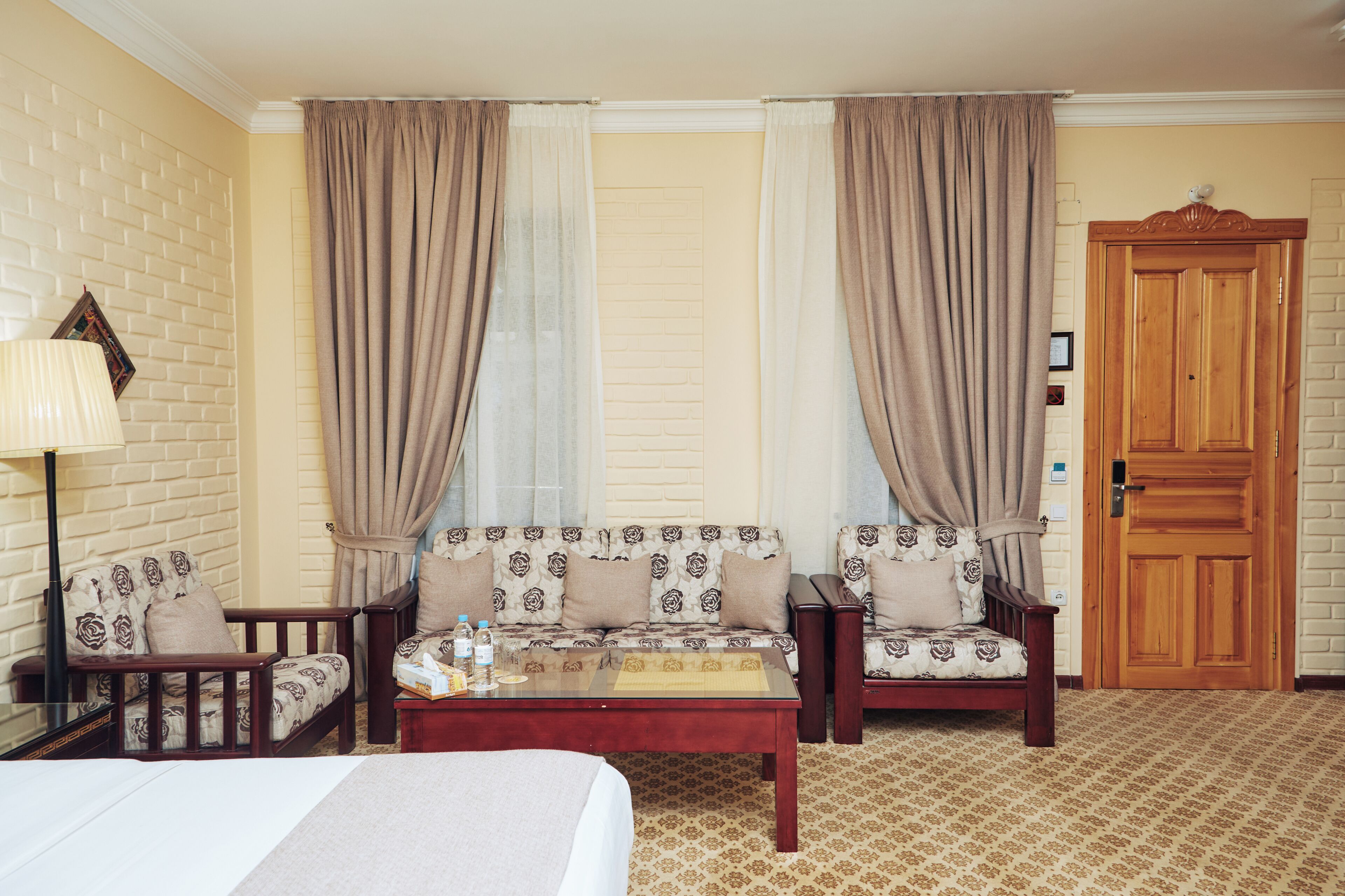 Una habitación de hotel con una cama, dos sofás, una mesa de centro, una lámpara y una puerta de madera.