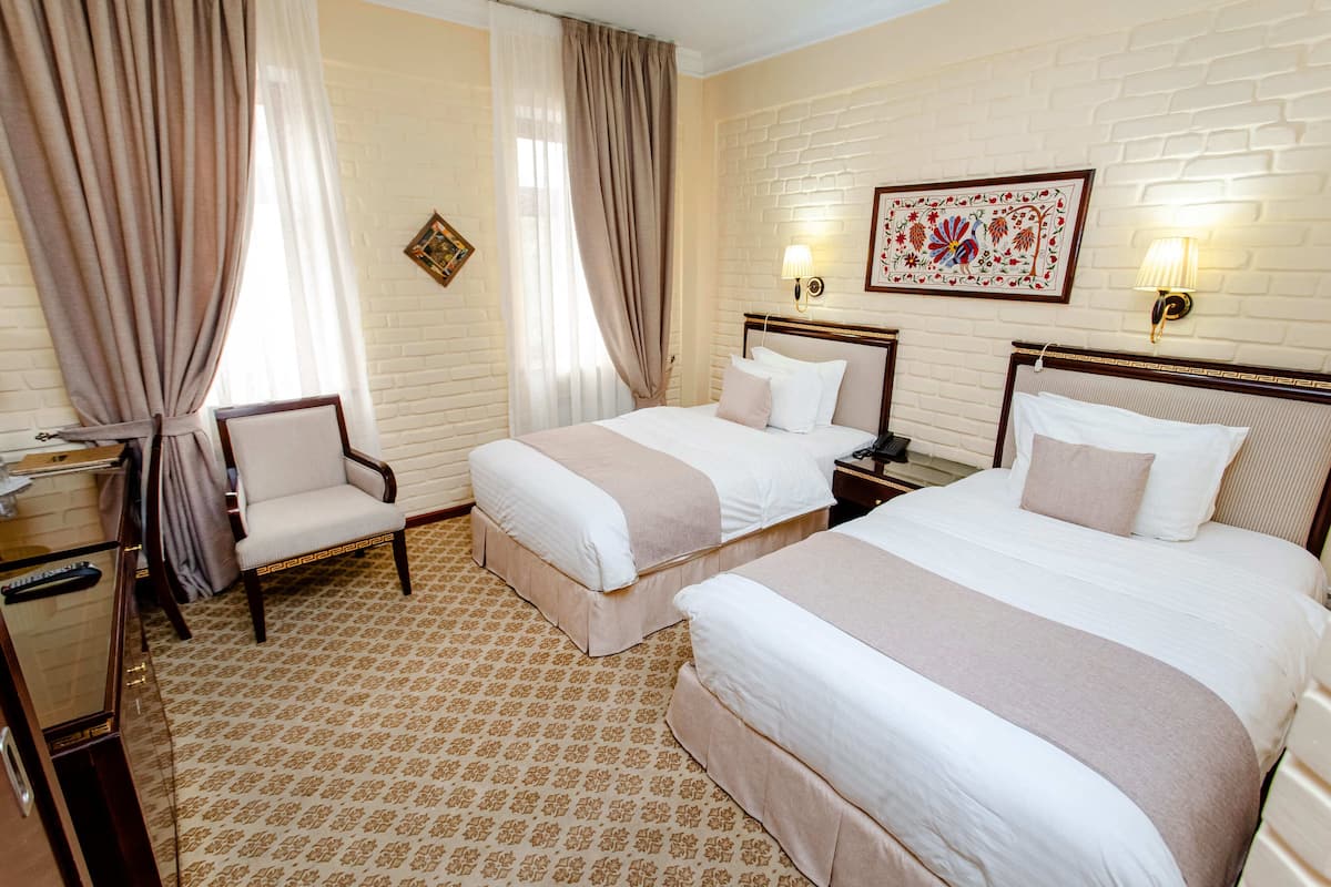 Une chambre d’hôtel avec deux lits, une chaise, un bureau et une lampe.