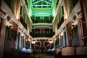 Un vaste hall d’hôtel à plusieurs niveaux, doté d’un plafond haut, de décorations en briques ouvragées et d’un escalier central.
