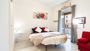 Un dormitorio con cama, sofá rojo, una mesita con lámpara y un cuadro en la pared.