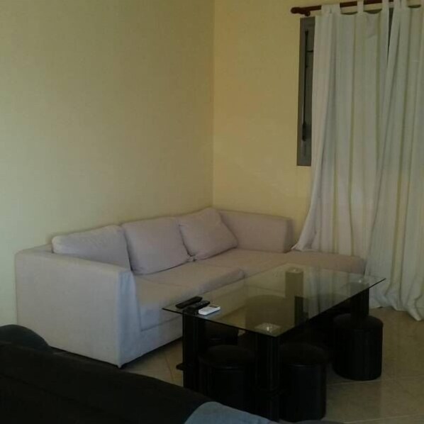 A living room with a sofa, a glass coffee table, and a window with curtains.