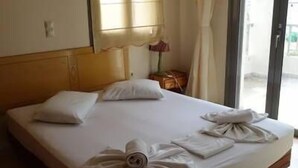 Een hotelkamer met een groot bed, een raam met gordijnen, een nachtkastje met een lamp en uitzicht op de omgeving.