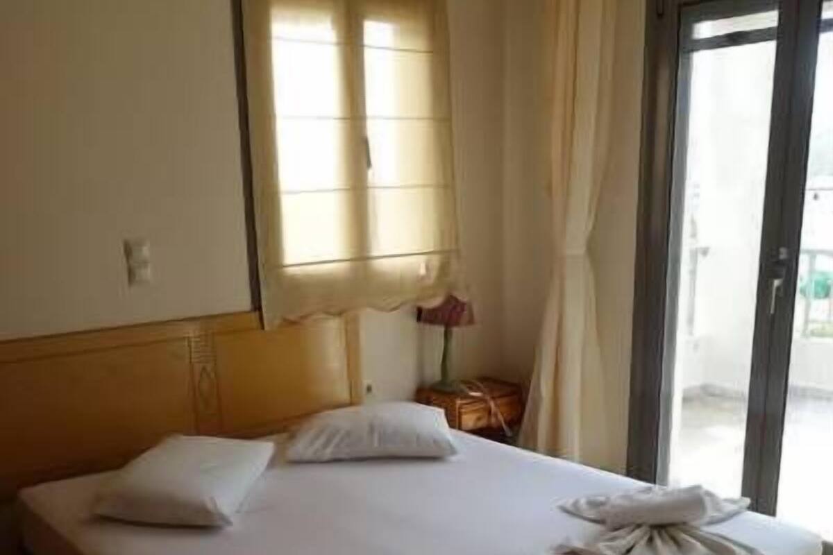 Une chambre d’hôtel avec un grand lit, une fenêtre avec des rideaux, une table de chevet avec une lampe et une vue sur l’extérieur.