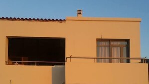 Een gebouw met twee verdiepingen, een balkon, een schuifdeur en een klein terras met tuinmeubilair.