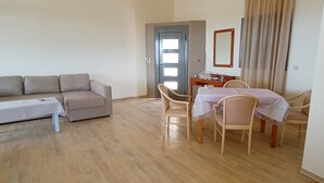Een woonkamer met een bank, een eettafel met stoelen en een deur.
