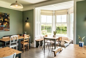 Un coin repas avec une baie vitrée, des tables et des chaises en bois, et une plante en pot.