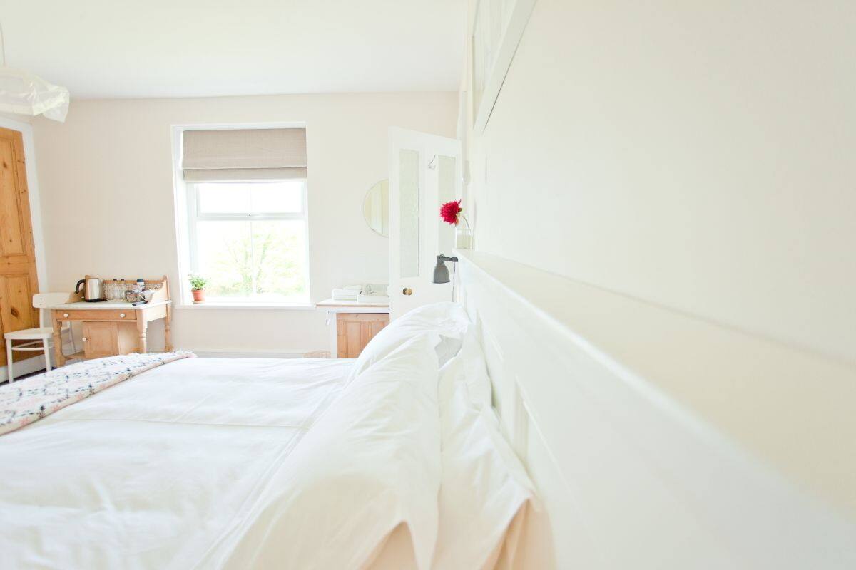 A bedroom with a bed, a desk, a window, and a mirror.