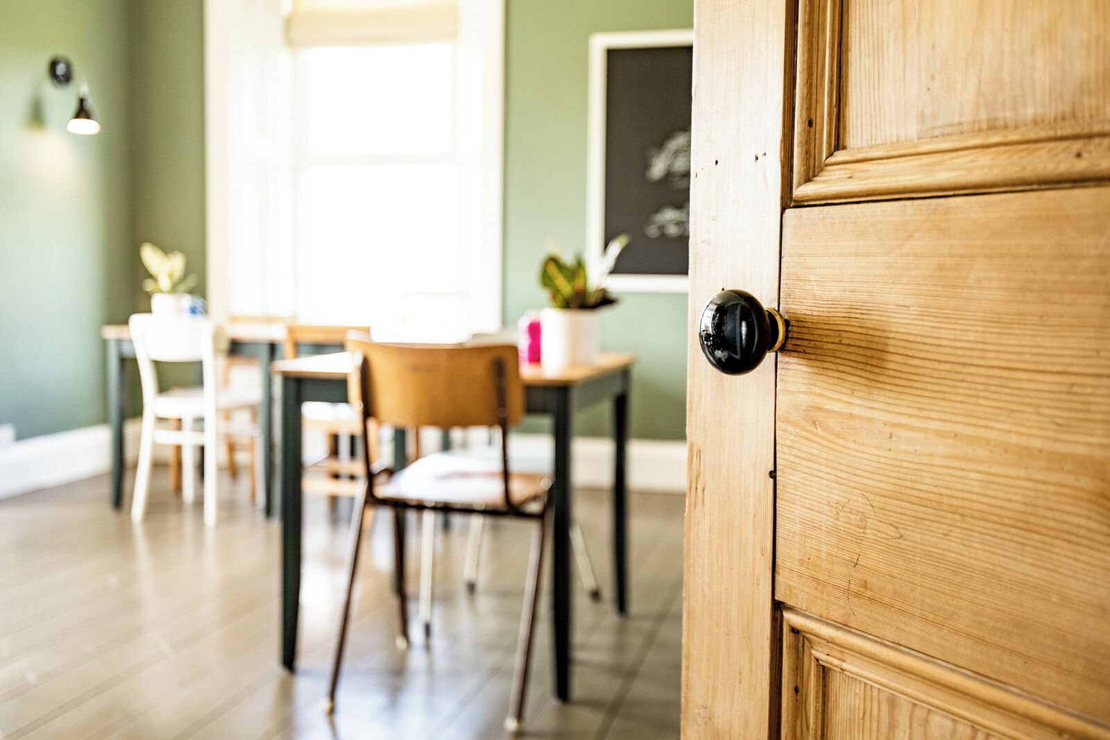 A wooden door with a round handle, a dining area with chairs and a table, and a window with blinds.