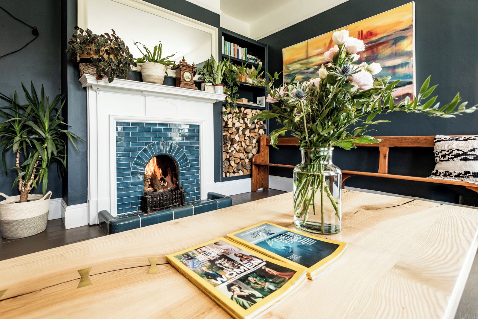 Un salón con chimenea, estanterías, un florero con flores y una revista sobre la mesa.