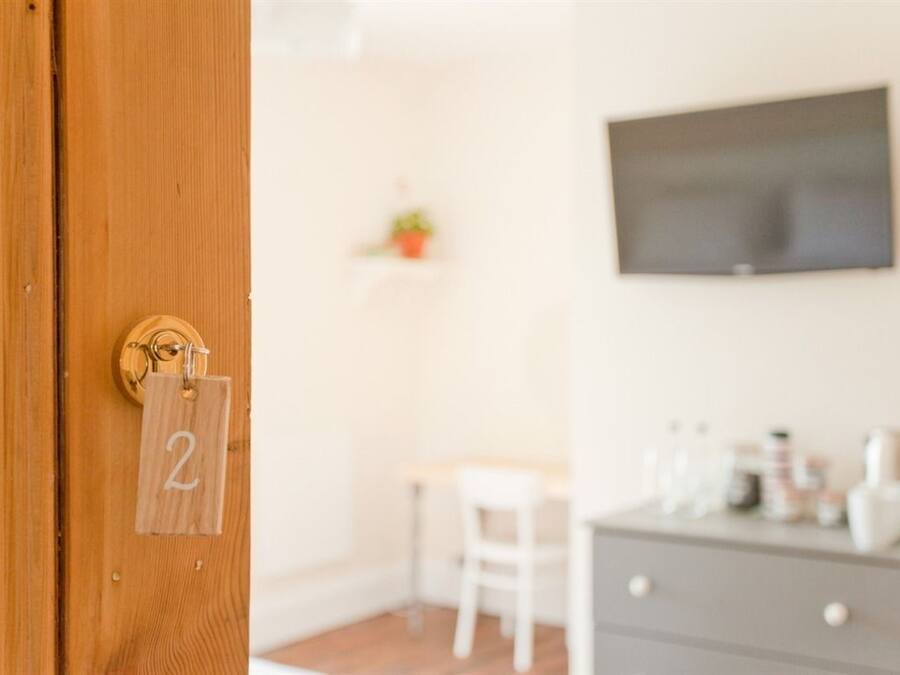 A room with a wooden door labeled '2', a white chair, a small table, a grey dresser, and a mounted television.