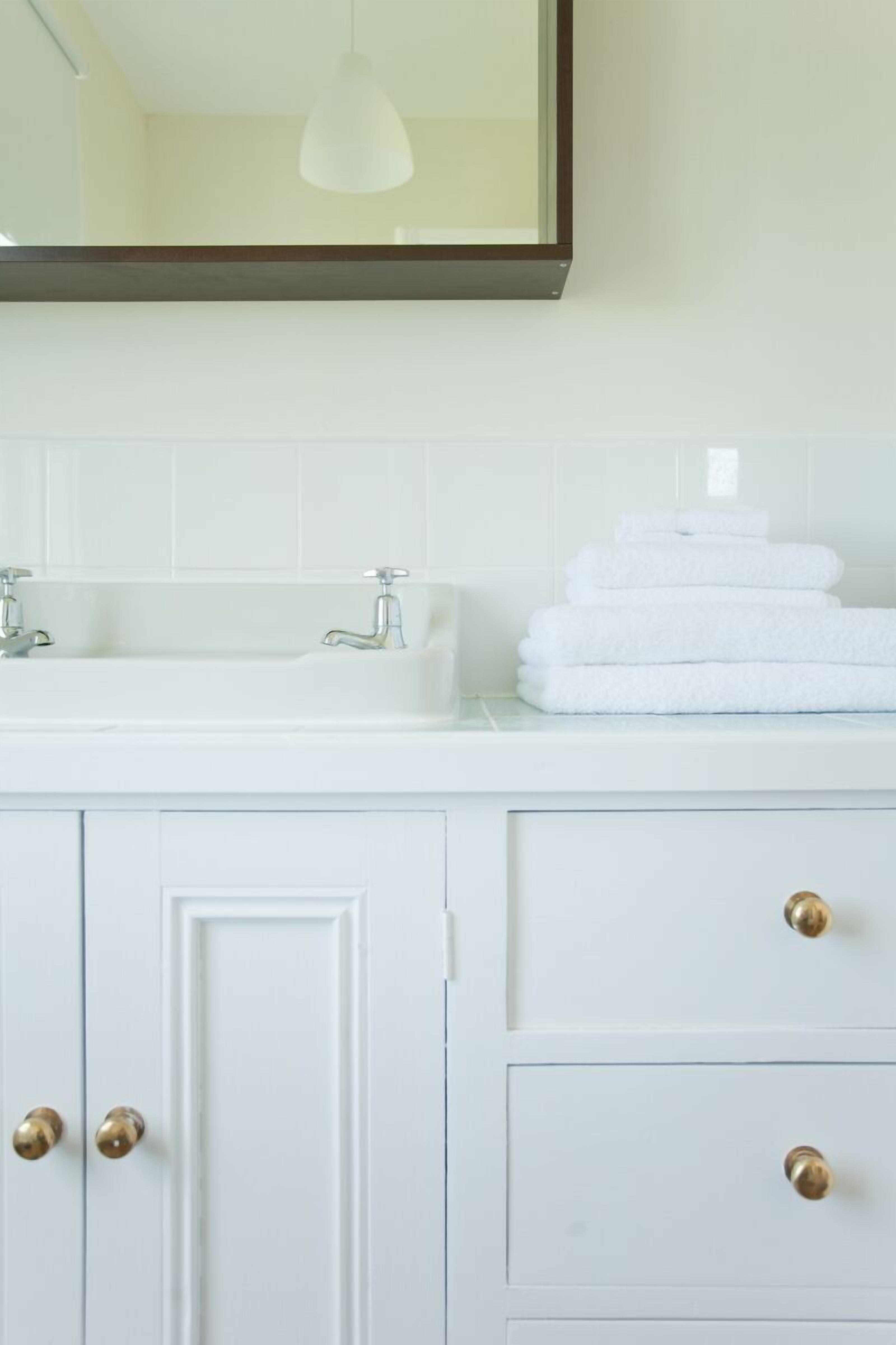 Un mueble de baño blanco con espejo, dos lavamanos y una pila de toallas blancas.