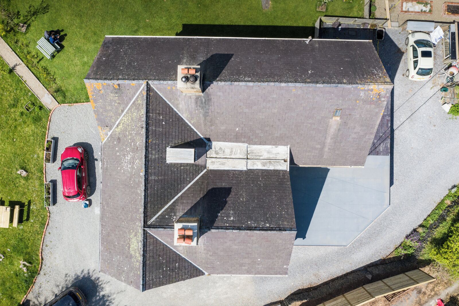 An aerial view of a residential building with a sloped roof, a driveway, and a red car parked on the street.