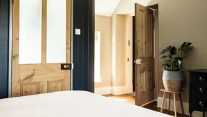 A bedroom with a large window, a wooden door, a bedside table with a plant, and a dresser. - The Old Vicarage (Cardigan)