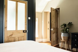Une chambre avec une grande fenêtre, une porte en bois, une table de chevet avec une plante et une commode.