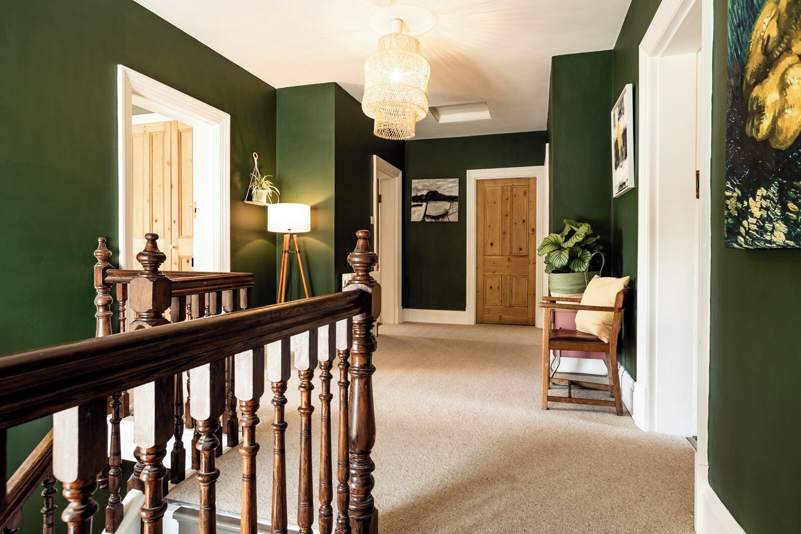 Un pasillo con paredes verdes, una escalera de madera, una lámpara de pie y una puerta que da a otra habitación.