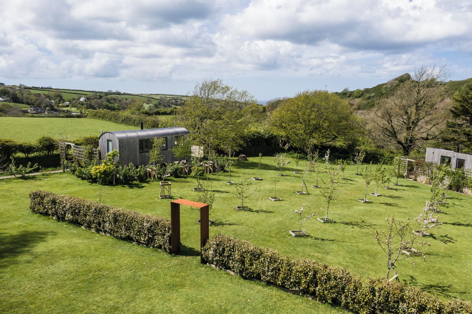 A rural landscape with a modern house surrounded by a well-maintained garden and a few trees.