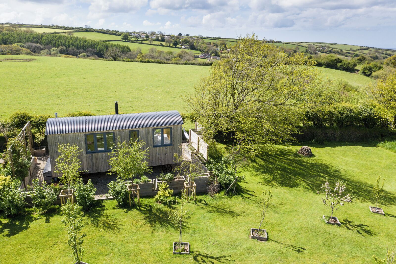 A wooden cabin with a metal roof, surrounded by a well-maintained garden and a rolling green landscape.