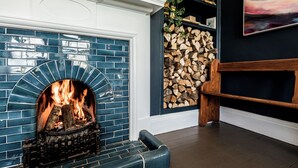 A fireplace with a blue-tiled surround, a stack of firewood, and a wooden bench. - The Old Vicarage (Cardigan)